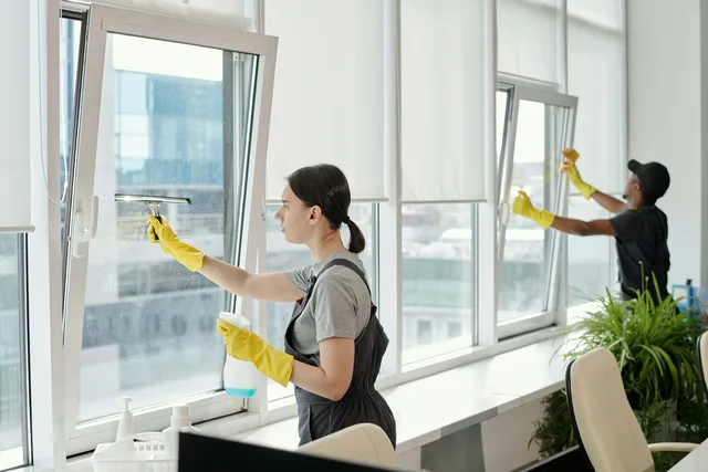 Cleaners washing interior office windows with a squeegee and cloth