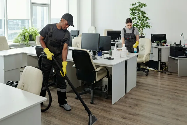 A cleaner vacuuming an office floor around desks and chairs